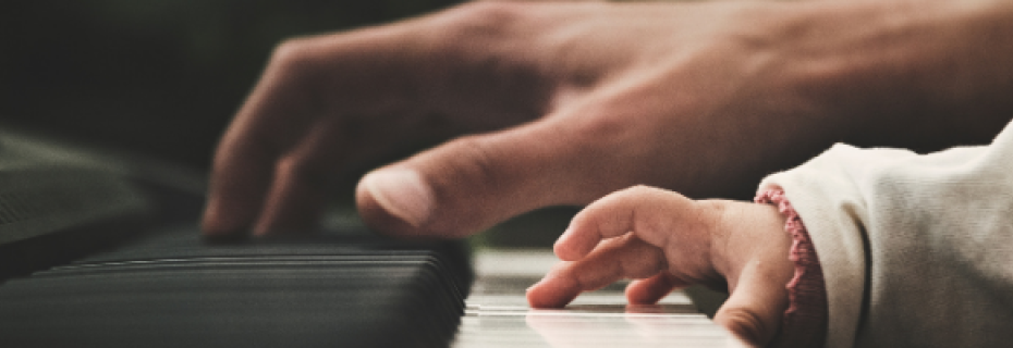 Hand of parent playing piano next to child's hand